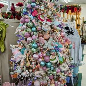 Candy themed artificial tree with various candy themed ornaments, picks, ribbons, and other accessories. At the base of the tree, there are candy themed decorations, nutcrackers, and presents.